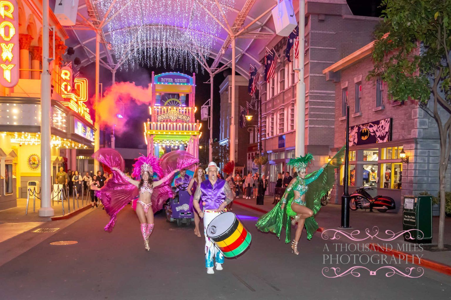 Parade with performers in colorful costumes and a drum, lit street at night.