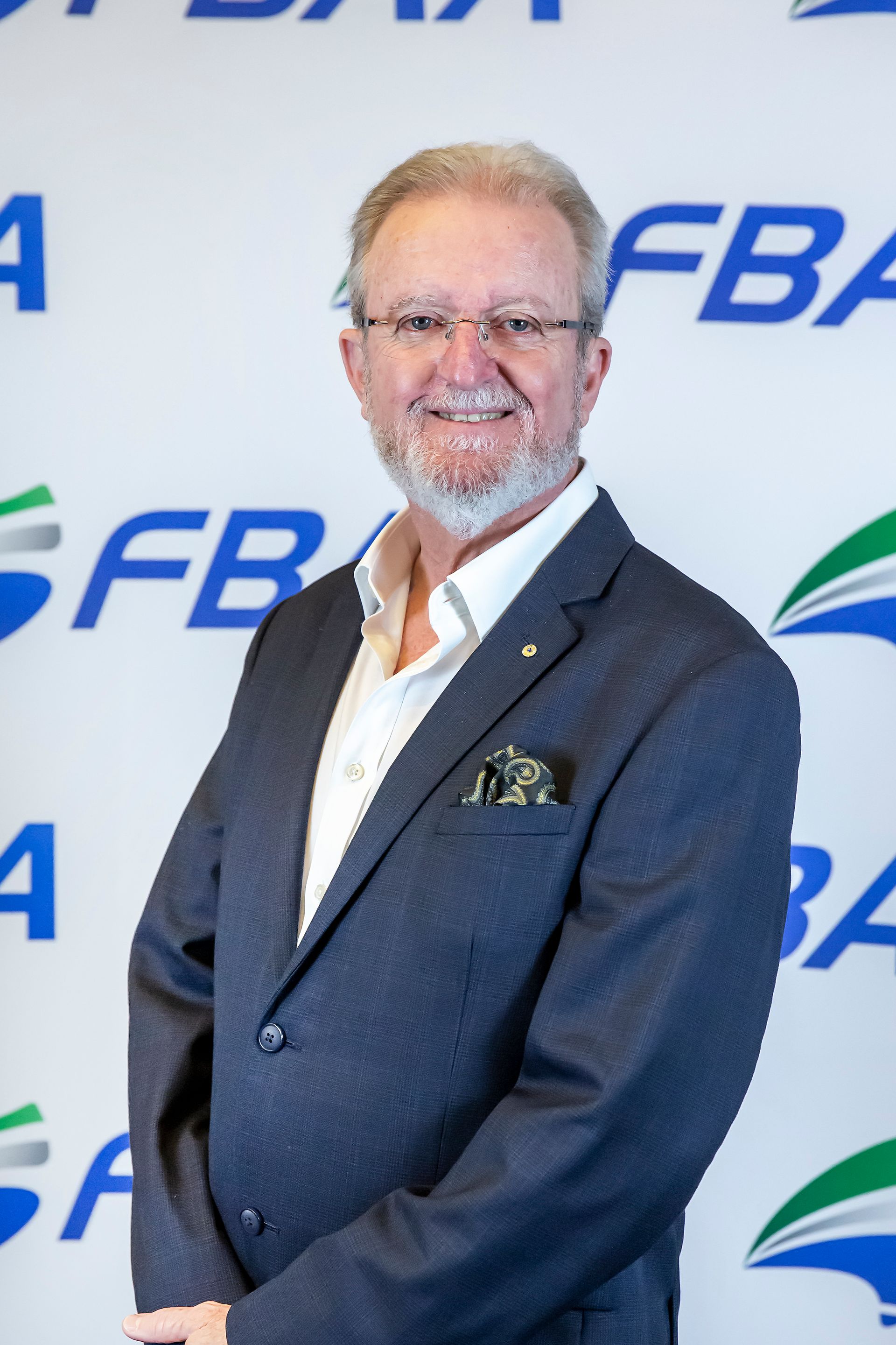 Man in blazer smiling, standing in front of a backdrop with an 