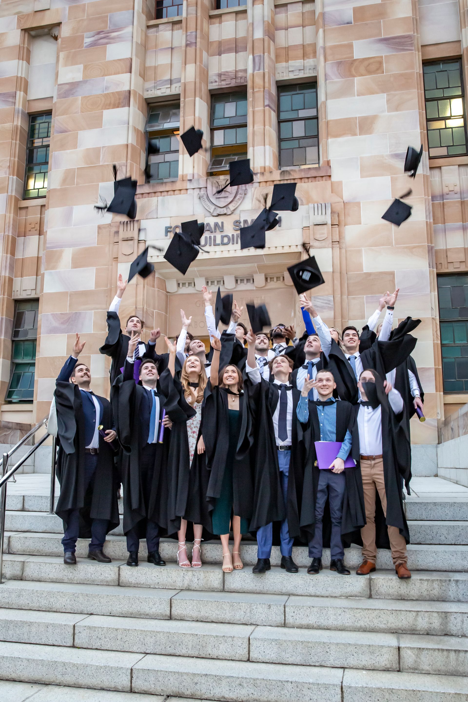 Graduates in caps and gowns throwing hats in the air in front of a stone building.