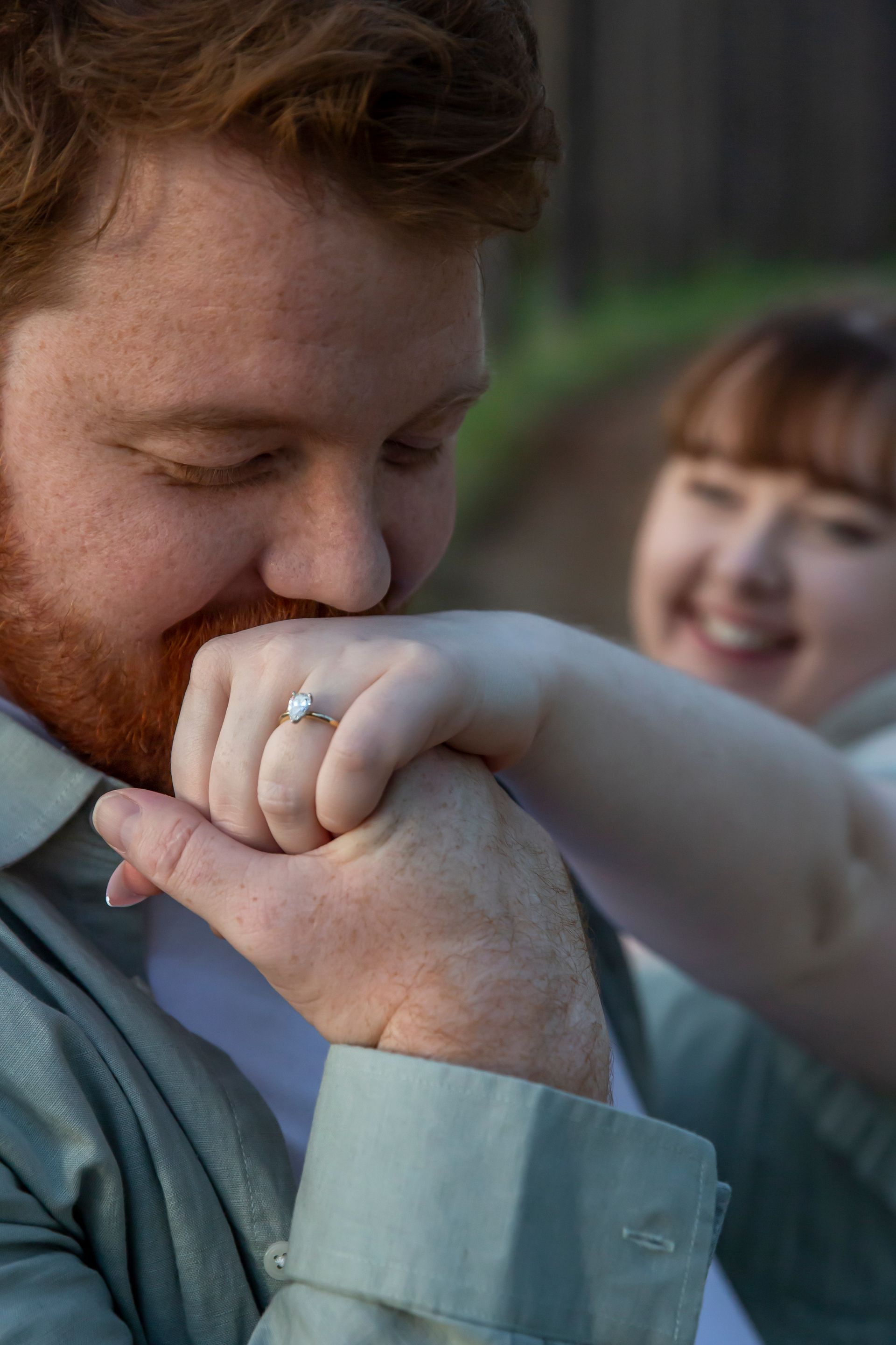 Man kissing hand of smiling woman, both embracing. She has an engagement ring.