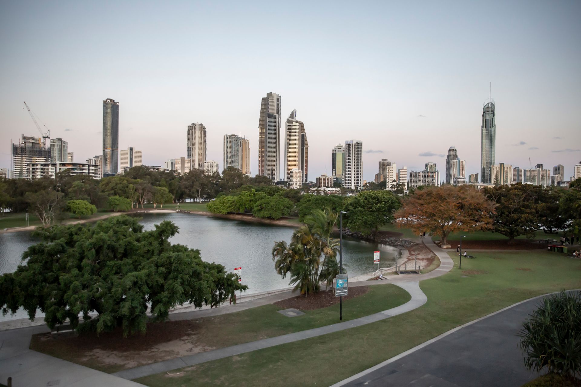 City skyline with skyscrapers and lake, park with trees, walkway, and clear sky. Photography by Andy Williams