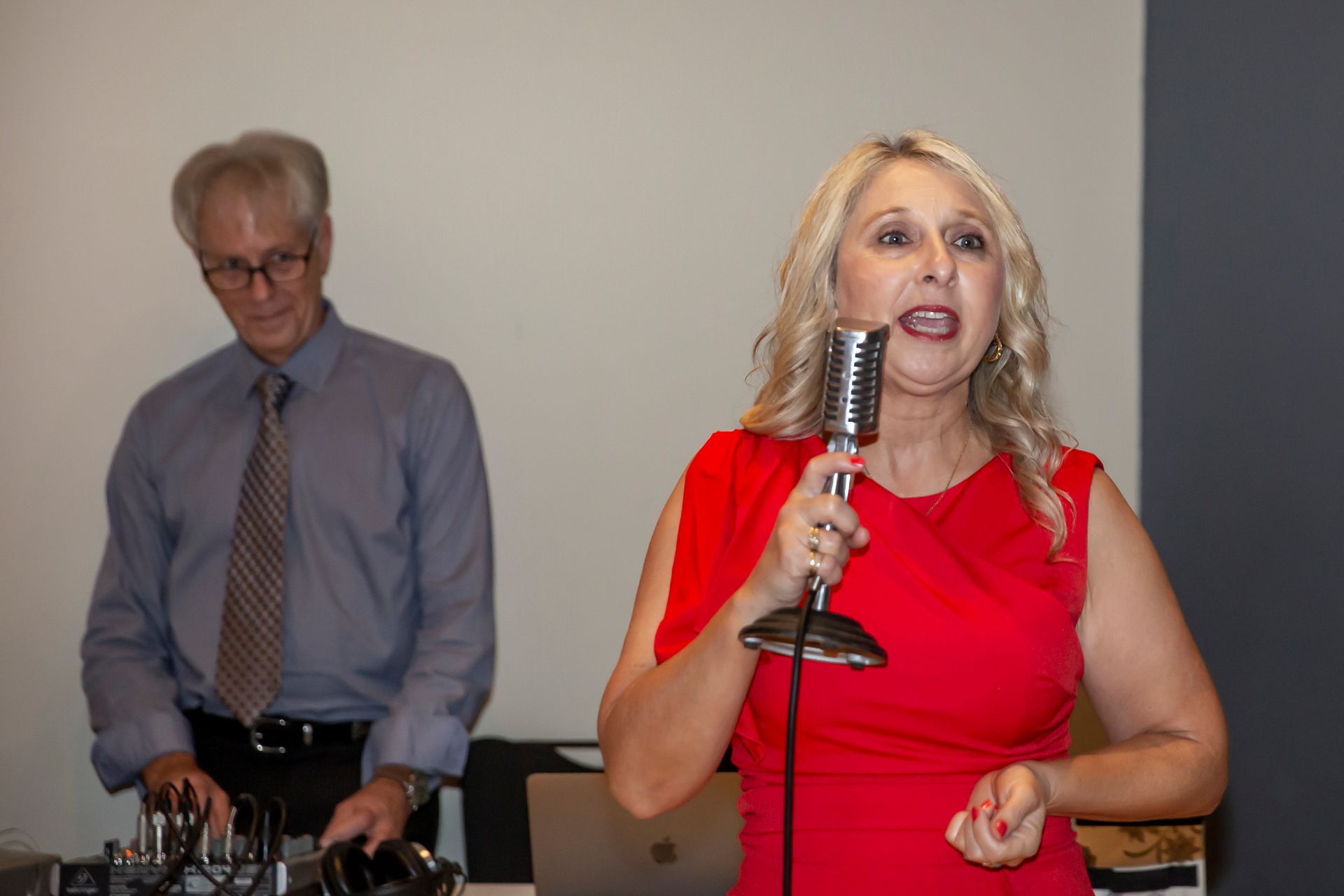 Woman in red dress singing into a vintage microphone; man at a soundboard in background. Photography by Andy Williams