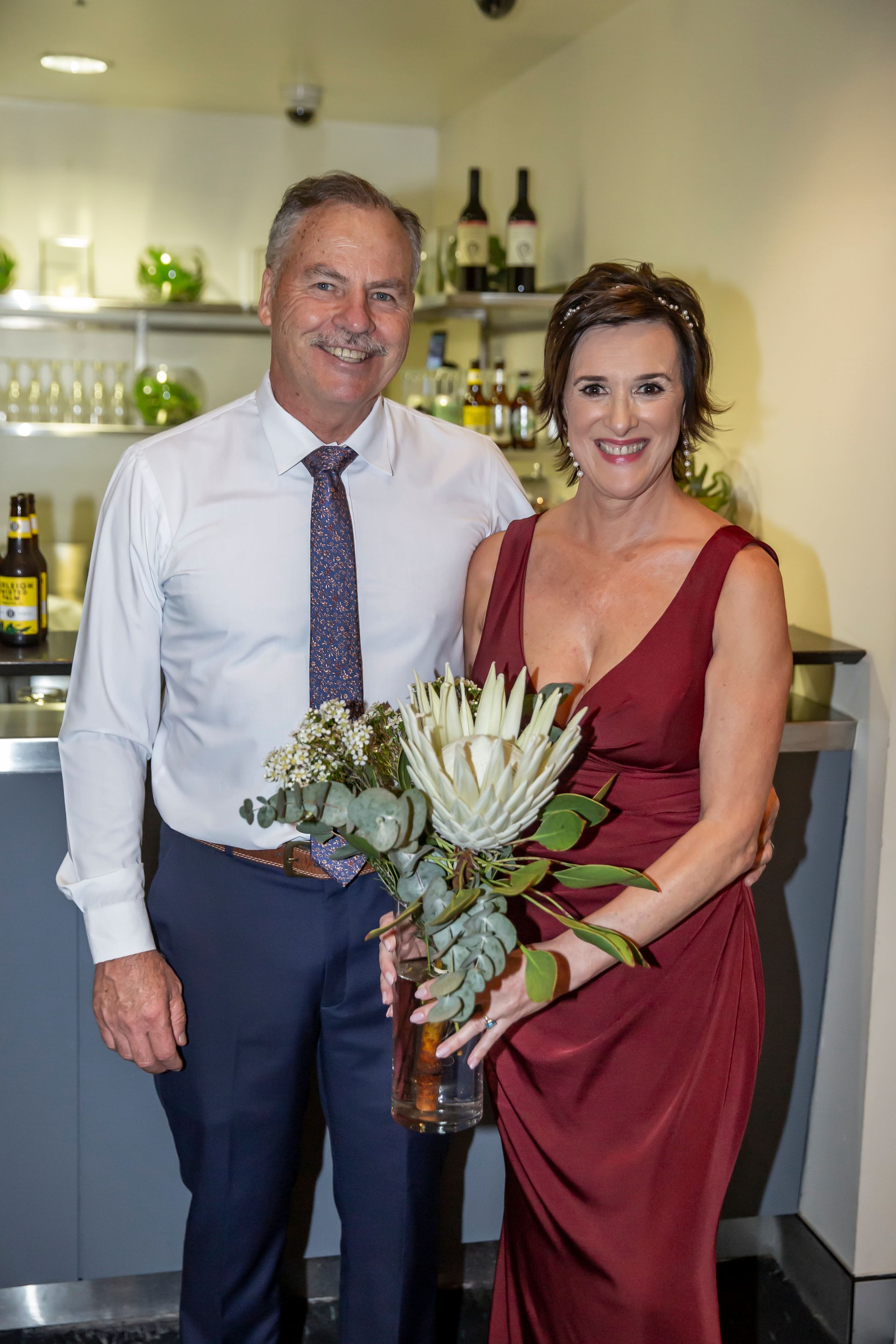 Couple in formal attire smiling, woman holding flower bouquet. Photography by Andy Williams