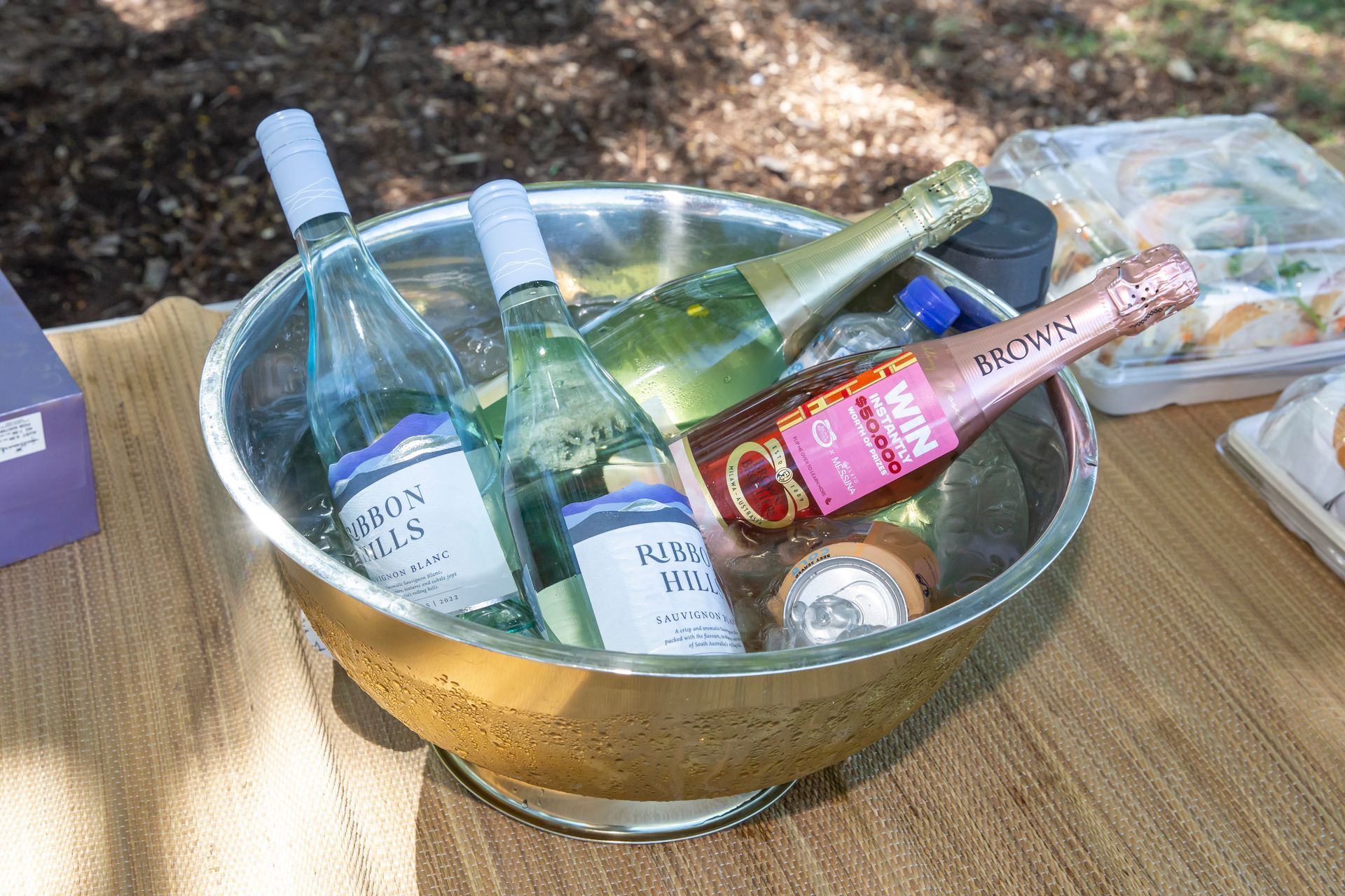 A metal bowl with chilled wine and champagne bottles on an outdoor table.