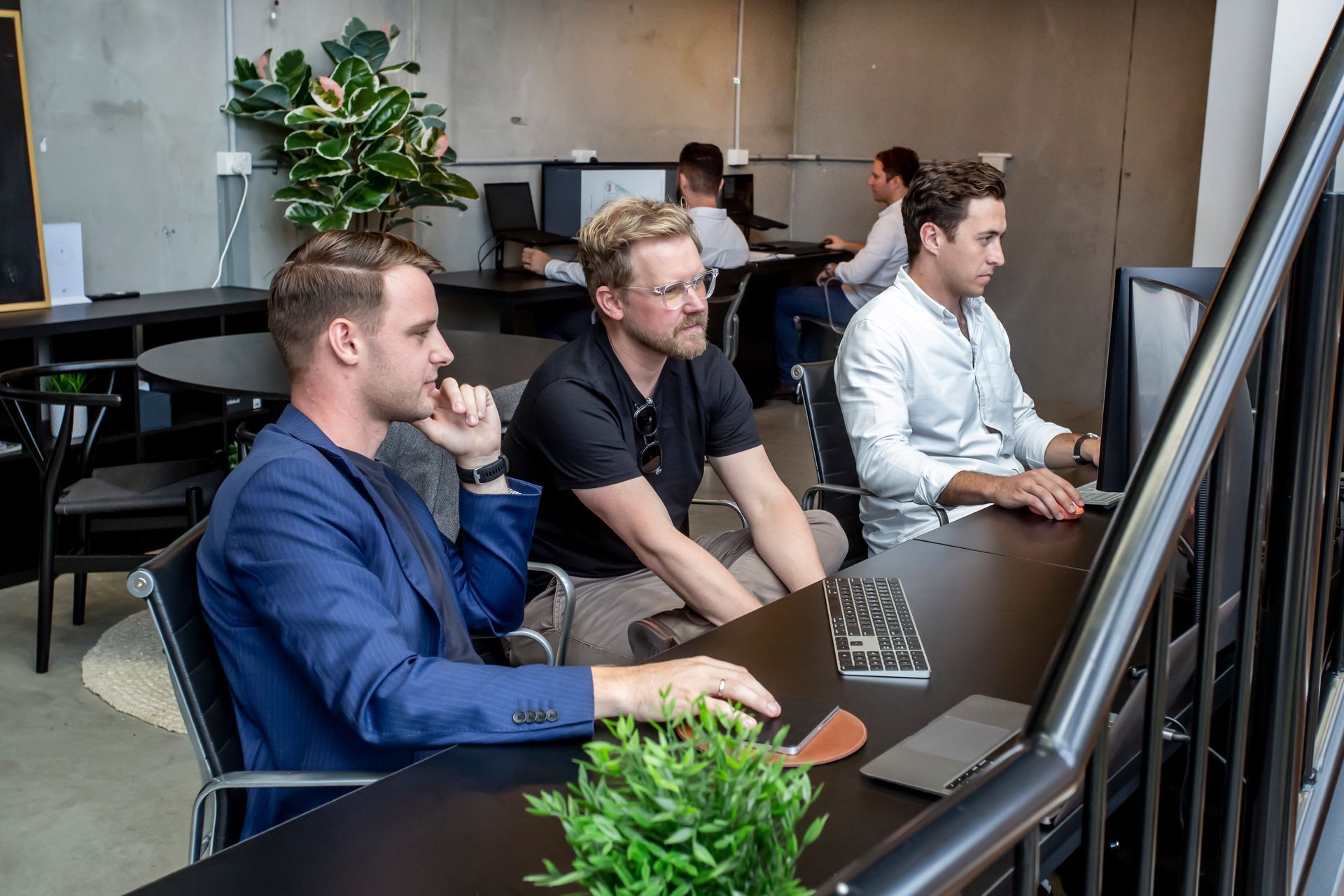 Men in an office working on computers, one man on the phone, modern interior with a staircase.