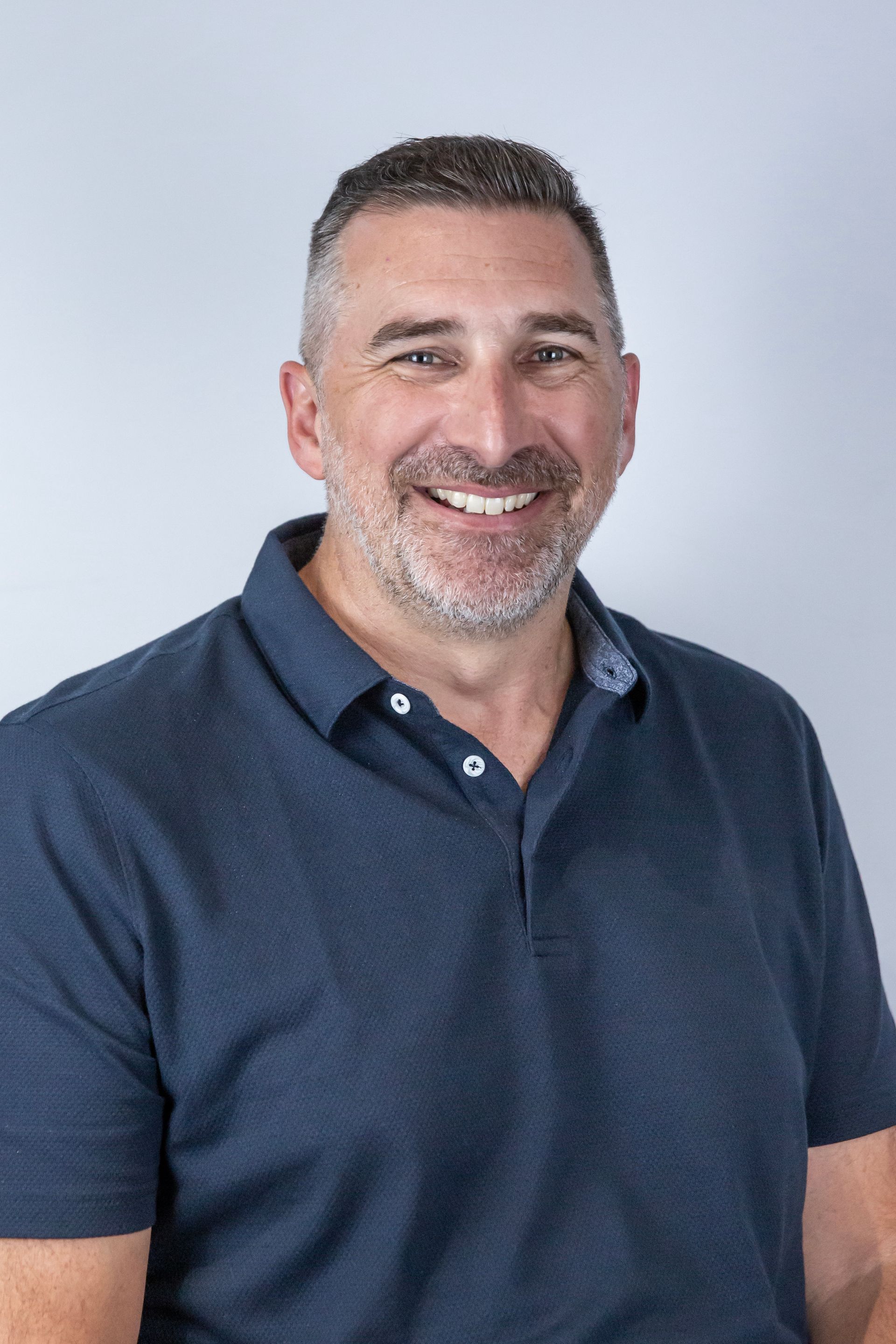 Man in blue polo shirt smiles, posing against a neutral gray backdrop.