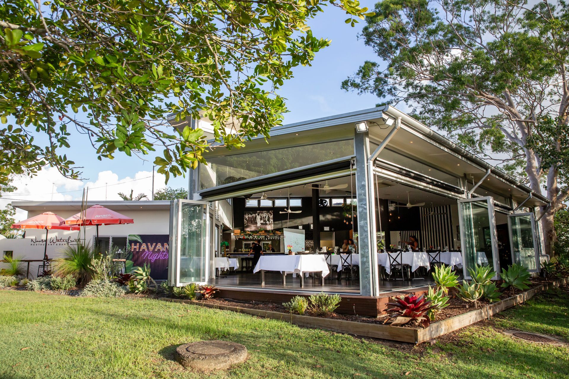 Restaurant with open walls, tables set, on a grassy area, under a retractable awning.