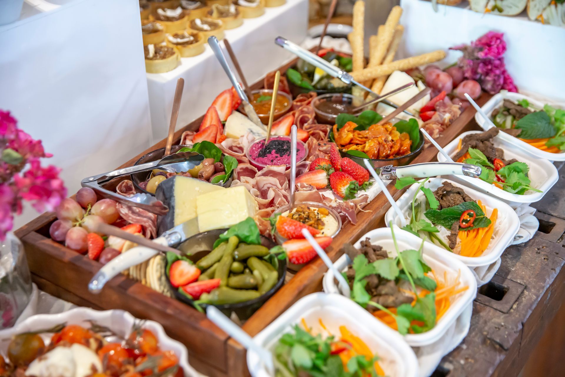 Charcuterie board with cheeses, meats, fruits, and salads, arranged on a wooden table for a party.