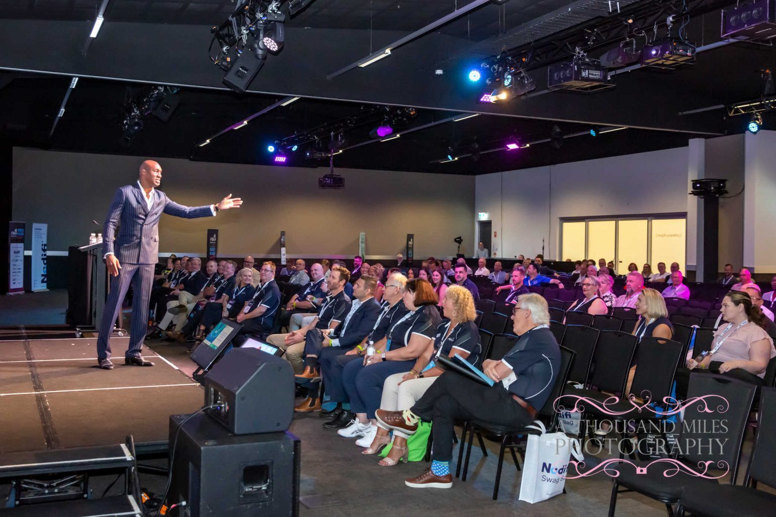 Man in suit giving presentation to seated audience in conference hall.
