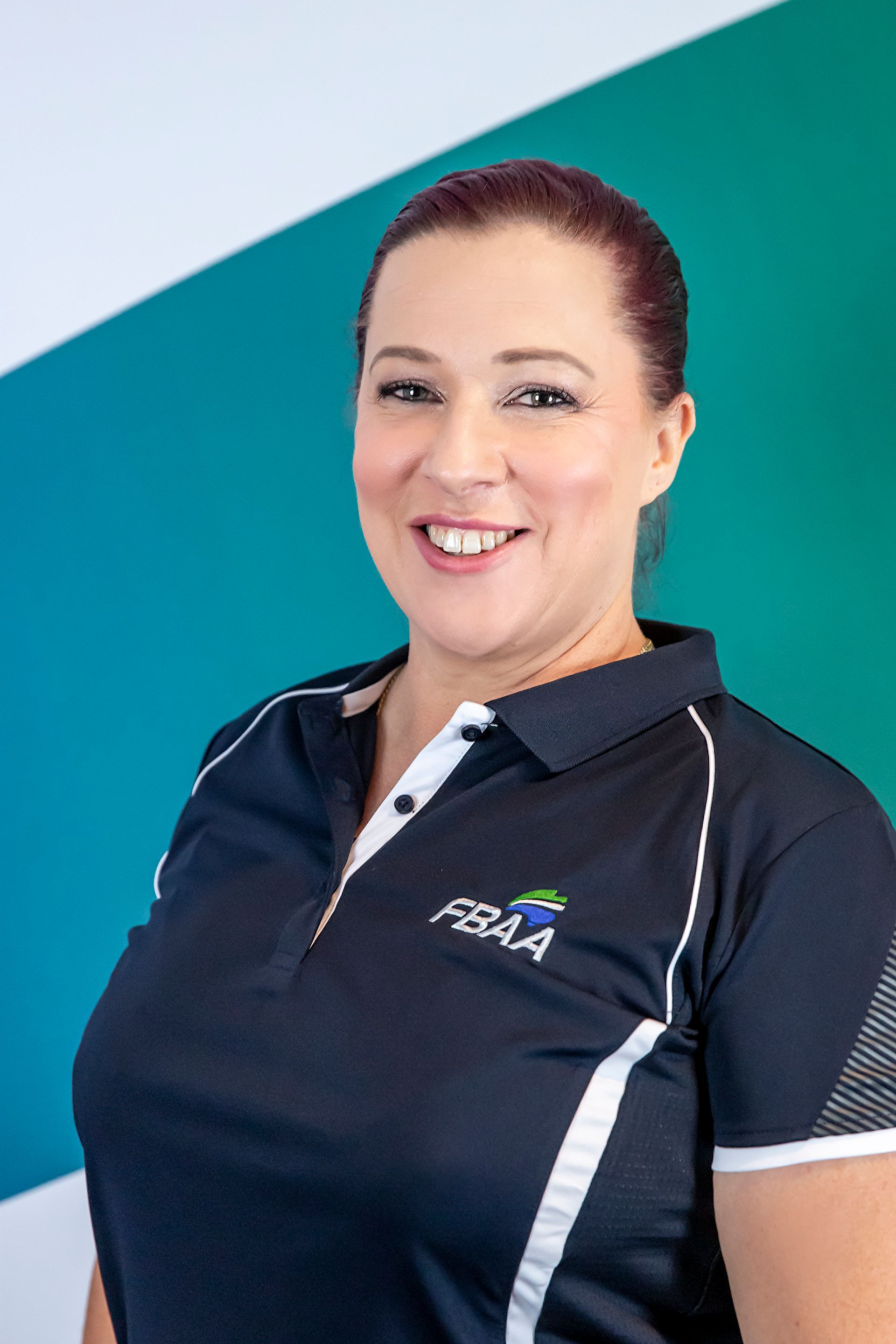 Woman in navy polo shirt with FBAA logo smiles, in front of turquoise and green background.