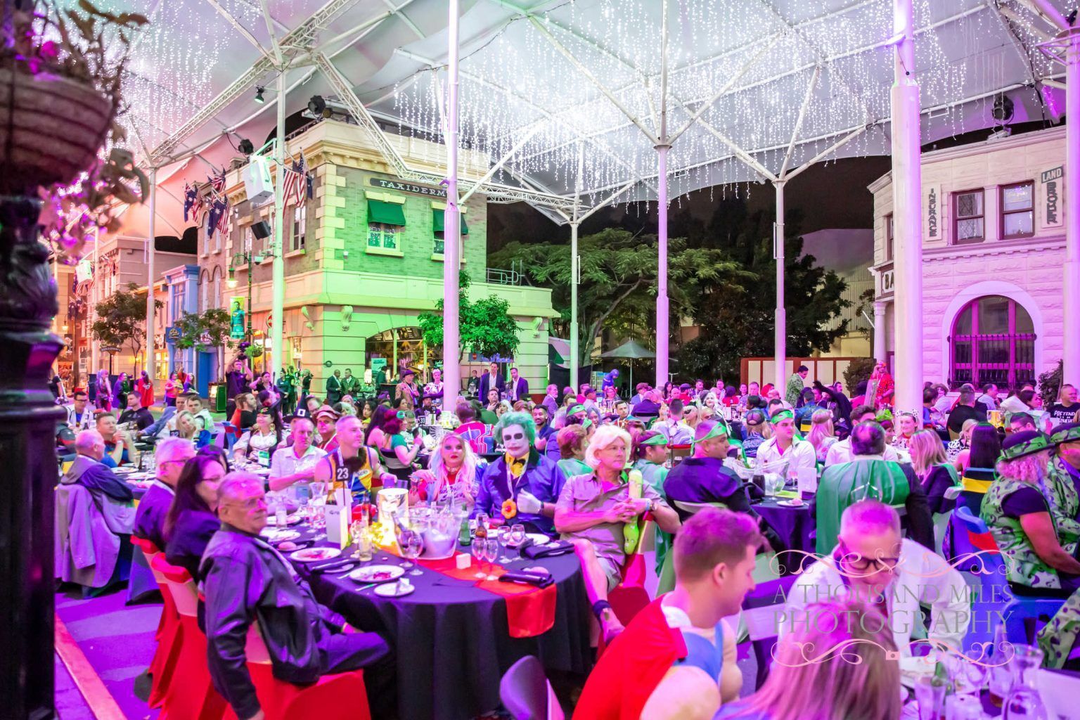 Large party at a banquet, in a decorated building with various people and tables, colorful lights above.