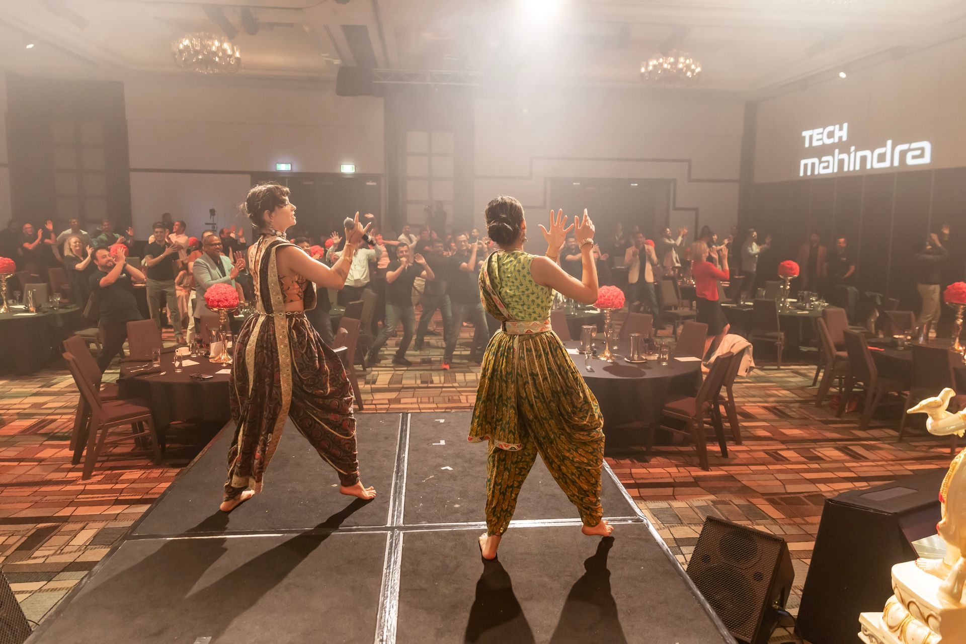 Two women in ethnic attire dance on stage at a Mahindra event.