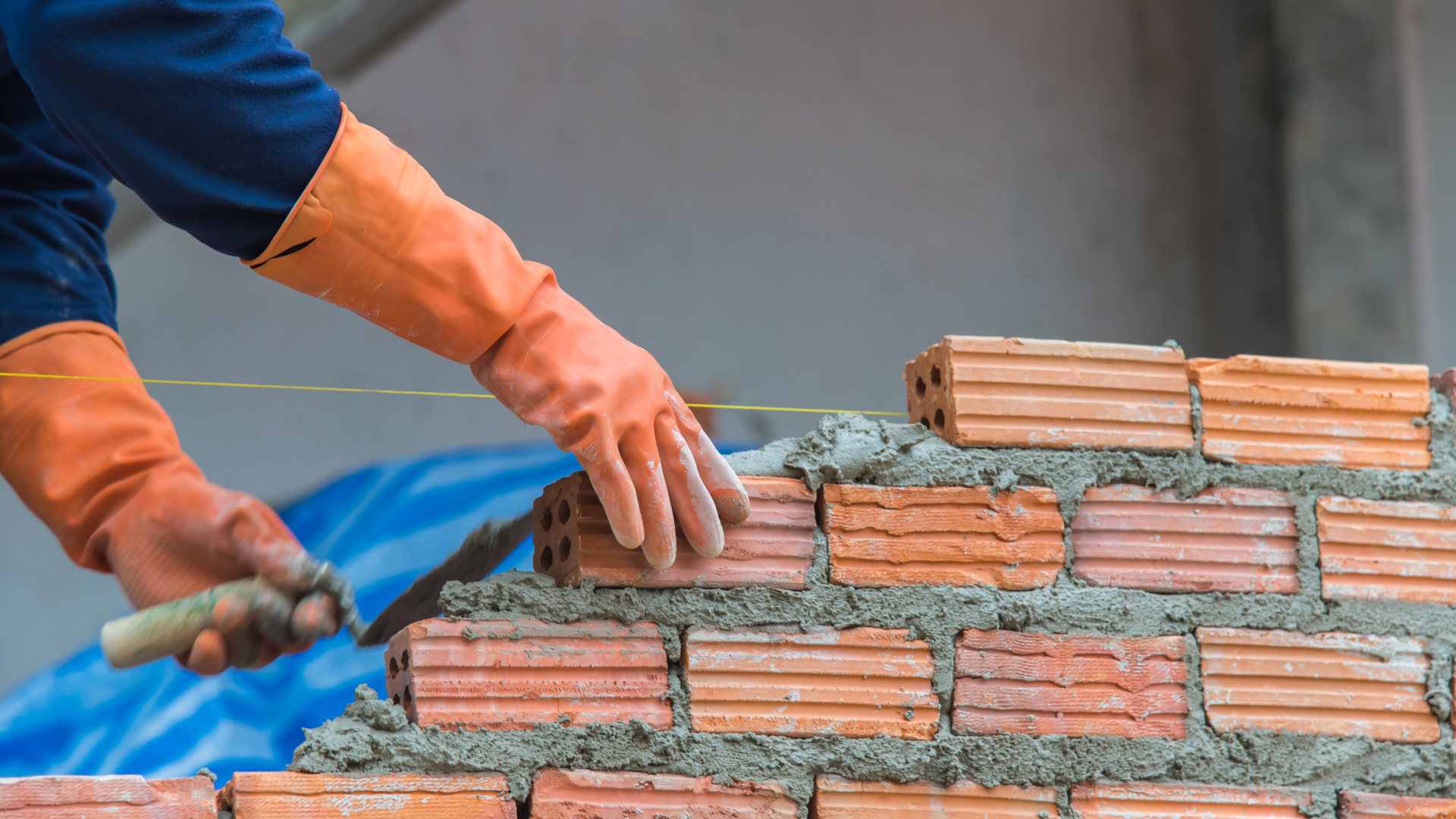Bricklayer using a trowel, wearing orange gloves, building a brick wall.