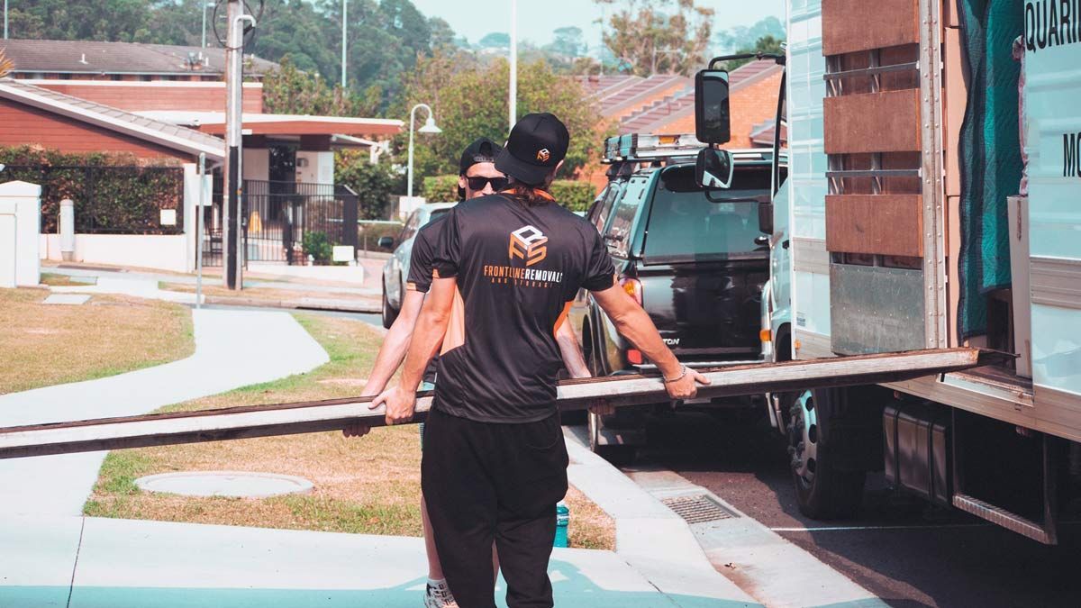 Two Men Are Loading A Large Wooden Plank Onto A Truck For Moving — Frontline Removals And Storage in Sydney, NSW