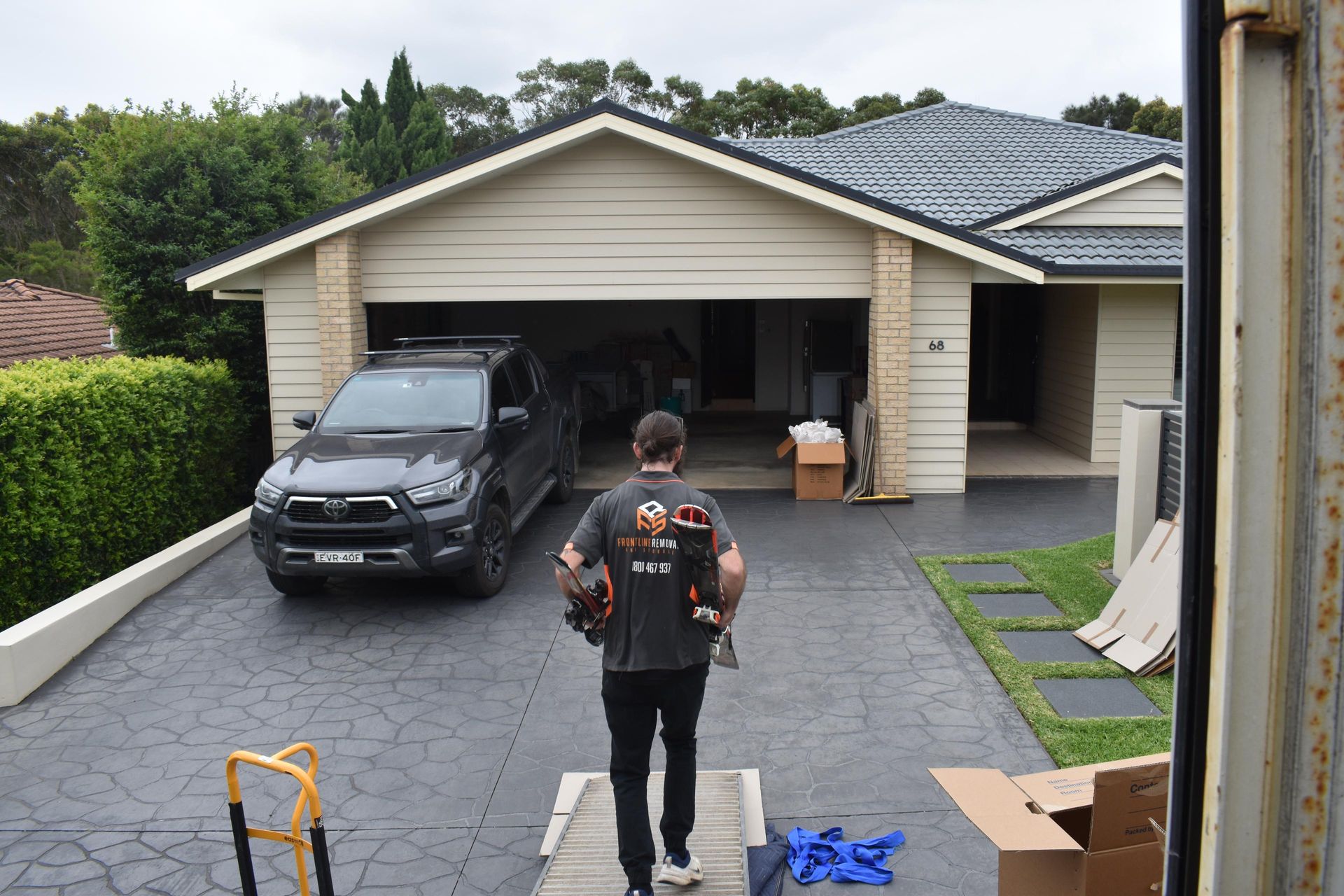 Man Carrying Items Walking Toward a Garage and House With a Car in the Driveway — Frontline Removals And Storage in Port Macquarie, NSW
