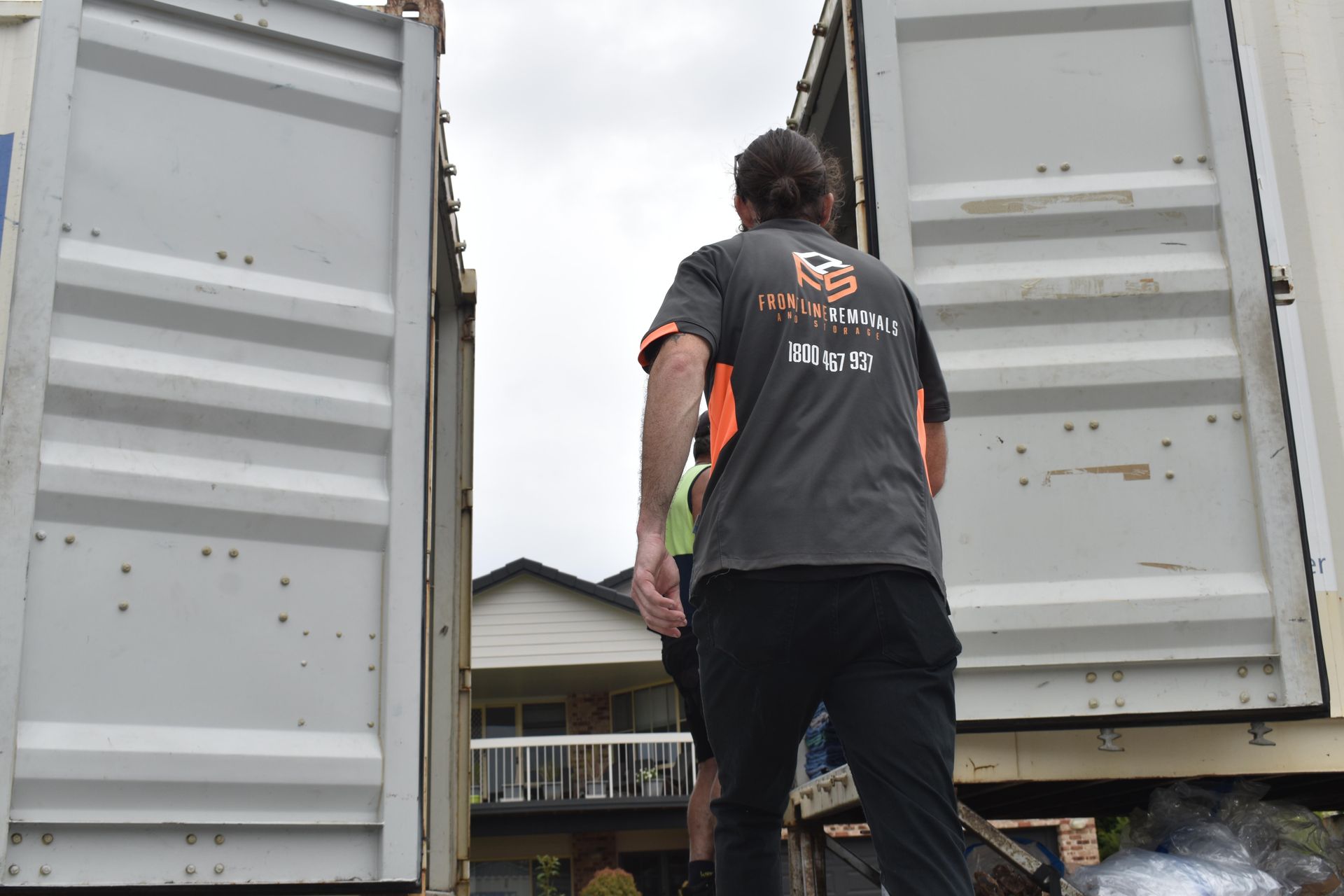 Man in a T-shirt Standing Between Two Open Shipping Containers — Frontline Removals And Storage in Port Macquarie, NSW