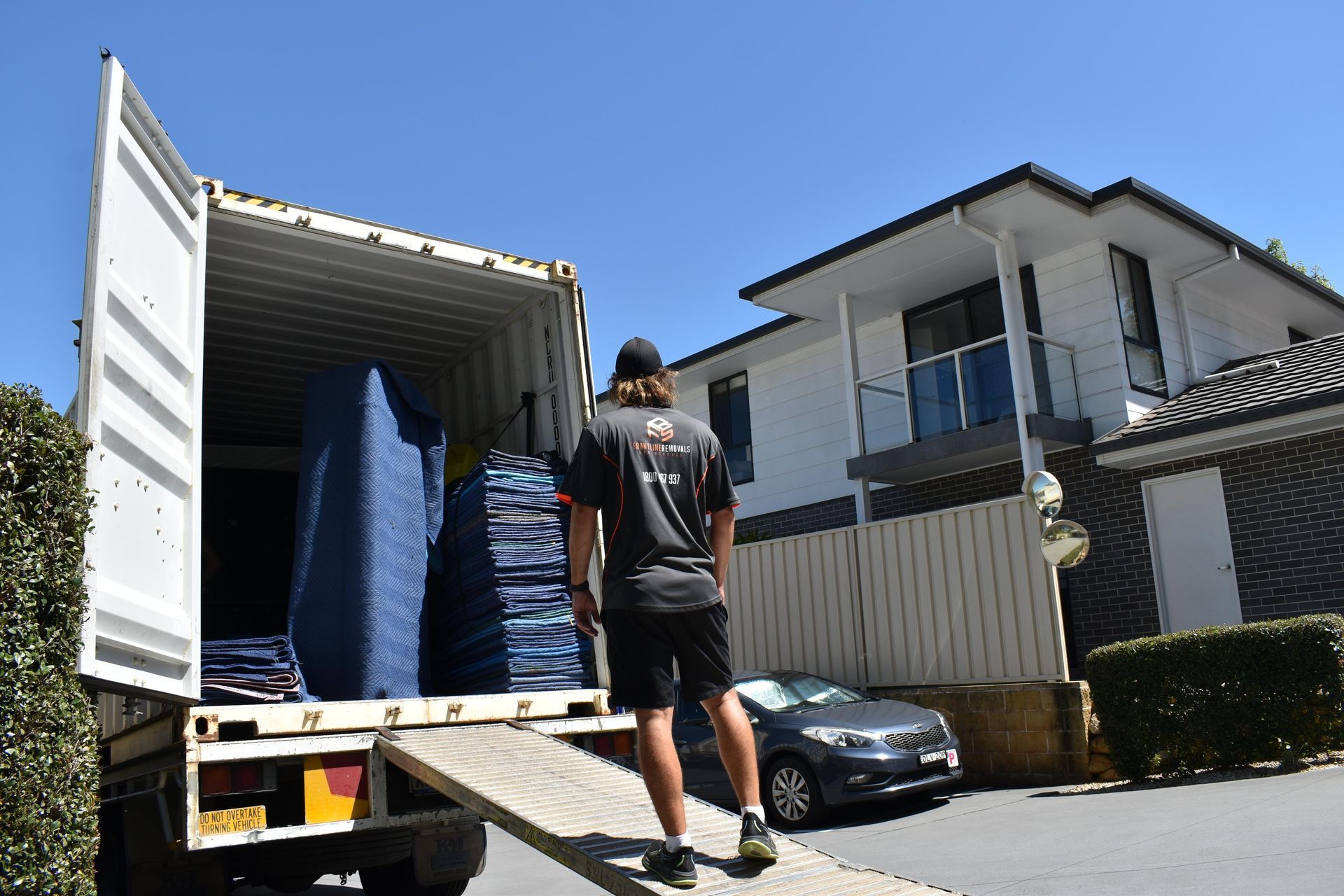Mover Loading a Truck With Household Items Near a Two-story House on a Sunny Day — Frontline Removals And Storage in Port Macquarie, NSW