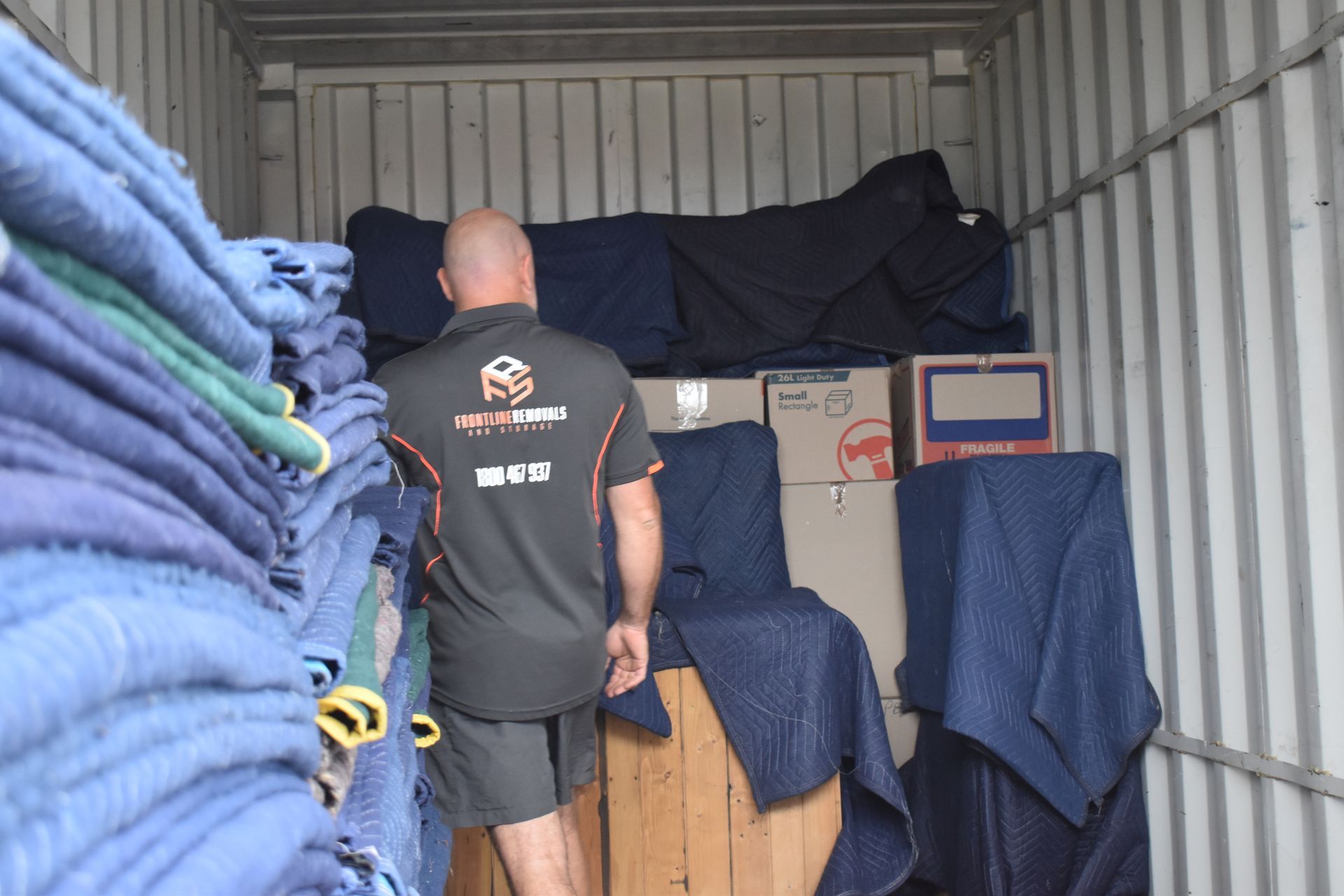 A Man And A Woman Are Carrying A Big Cardboard Box Up The Stairs — Frontline Removals And Storage in Port Macquarie, NSW