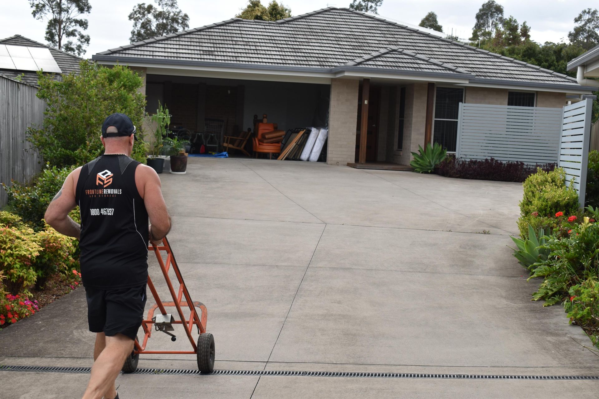 A Person in a Black Shirt is Pushing a Dolly Towards a House With an Open Garage — Frontline Removals And Storage in Port Macquarie, NSW