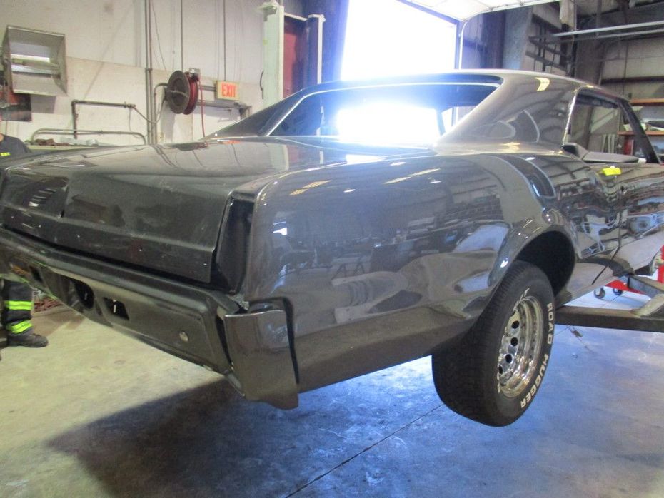 A partially restored gray classic car in a workshop, with a focus on the rear quarter panel and tire.