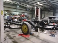 Car chassis with a yellow wheel in a workshop. Another car body is in the background.