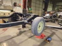 Car frame on blocks in a garage. Black frame, one wheel attached, gray tire, red blocks, dim lighting.