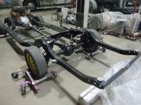 Black car frame with wheels in a workshop setting.