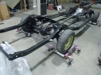 Black car frame on pink dollies, inside a shop. Wheels are attached.