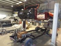 Car body elevated above its chassis in a workshop, undergoing restoration.