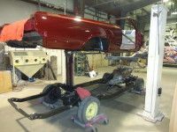 Red car body on a lift above a chassis in a workshop, undergoing restoration.