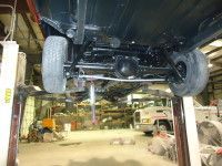 Undercarriage of a black car, raised on a lift in a garage, with large tires.
