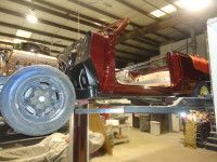 Red car frame on a lift in a garage, undergoing restoration.