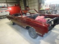 Burgundy convertible car in a garage with hood and top removed, under restoration.