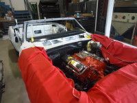 White car frame with red engine cover, engine visible, inside a garage.