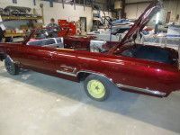Red convertible car with trunk open in a workshop. Yellow wheel and a person in the background.