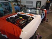 White classic car under restoration in a garage, engine exposed, red cover over body.