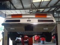 Classic white car with orange stripes, elevated on a lift in a garage.