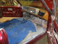 Red car interior, blue floor covering, light-colored dashboard, door open.