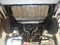 Underside of a car on a lift; showing the gas tank, exhaust, suspension, and rear tires.