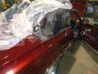 Red car part partially covered with plastic, in a garage setting.
