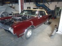 Maroon Oldsmobile convertible in a garage, hood open.