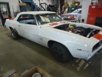 White classic car, partially restored, in a garage with orange racing stripe and hood open.