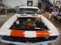 White classic car with orange stripes, engine exposed, in a garage.
