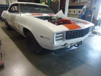 White 1969 Chevrolet Camaro with orange stripe, hood open, in a garage.