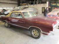 Maroon convertible car in a garage with a tan roof, golden wheels. Person standing in the background.