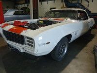 White 1969 Chevrolet Camaro in a garage, engine exposed, with orange racing stripes.