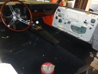 Interior of a classic car under restoration, with black carpet, steering wheel, and door panel.