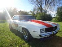 White 1969 Chevrolet Camaro SS with red racing stripes on grass, sun in the background.