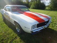 White 1969 Chevrolet Camaro SS with red stripes, parked on grass.