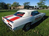 White convertible car with red and white stripes on the back, parked on grass.